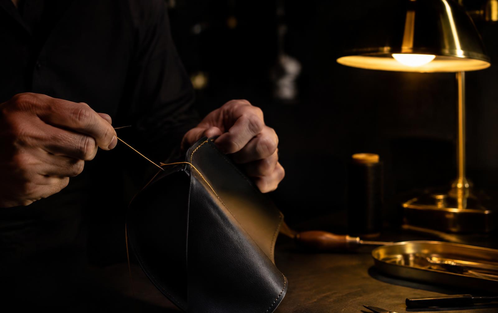 Artisan hands stitching black leather with gold thread